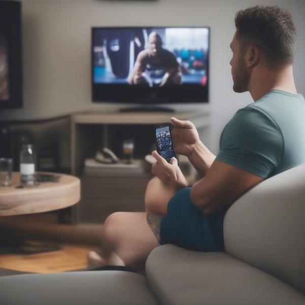 Man watching CrossFit games on TV with phone in hand checking updates